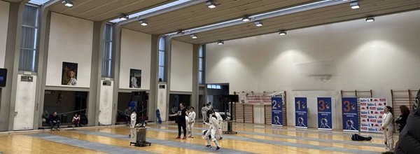 Atleti che si allenano su pedane di scherma in una sala indoor con giudici e pubblico